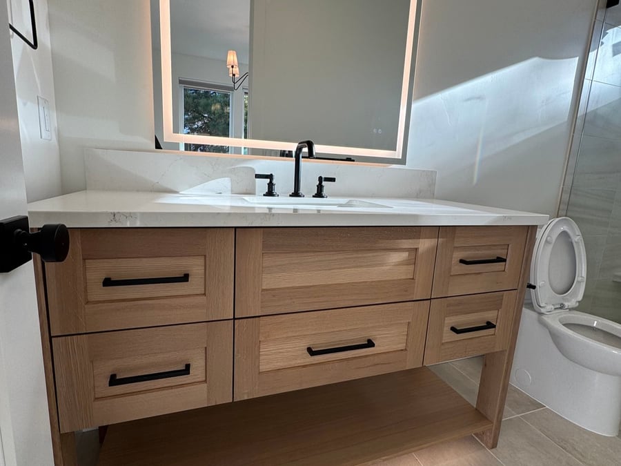 Light wood bathroom vanity with black hardware, a backlit mirror, and quartz countertop