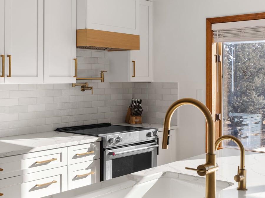 White shaker kitchen cabinets with brass hardware, a gold pot filler, and quartz countertops