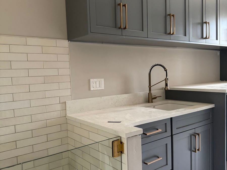 Charcoal gray laundry room cabinets with brass hardware and a utility sink